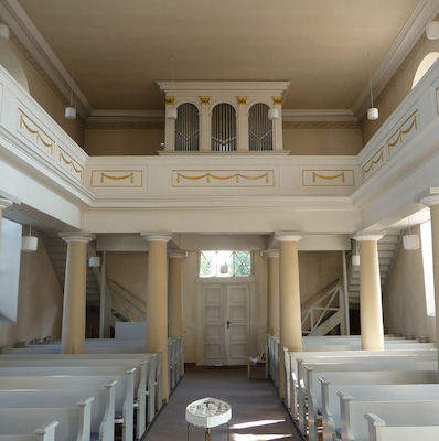 Ein Kircheninneres mit Kirchenbänken, einem Kanzel und einer Treppe.