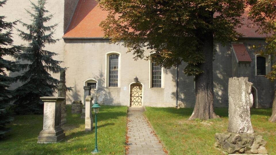 A stone pathway leading to a building with a red-tiled roof, surrounded by trees and a stone monument.