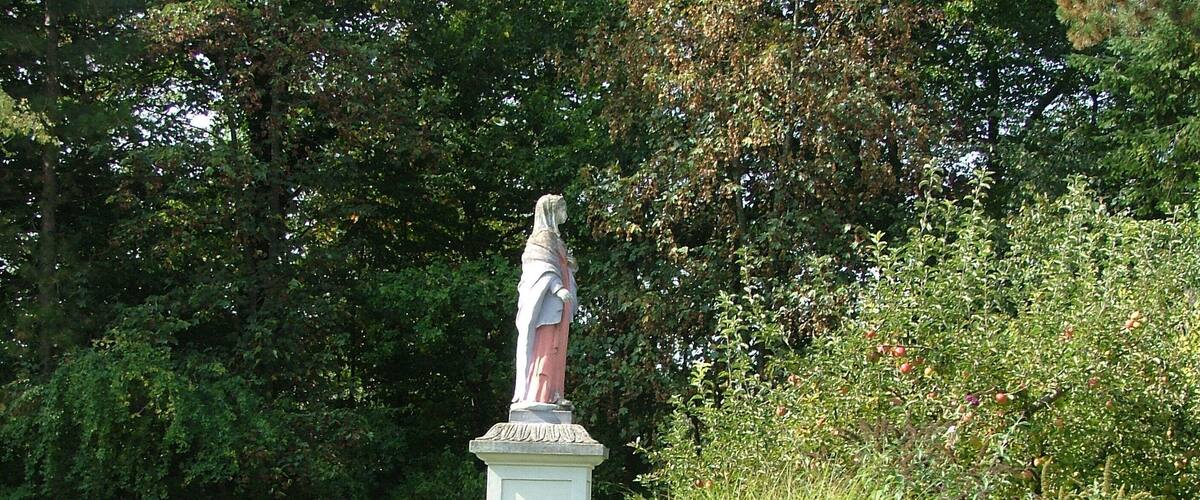 A statue in a garden with lush greenery and trees in the background.