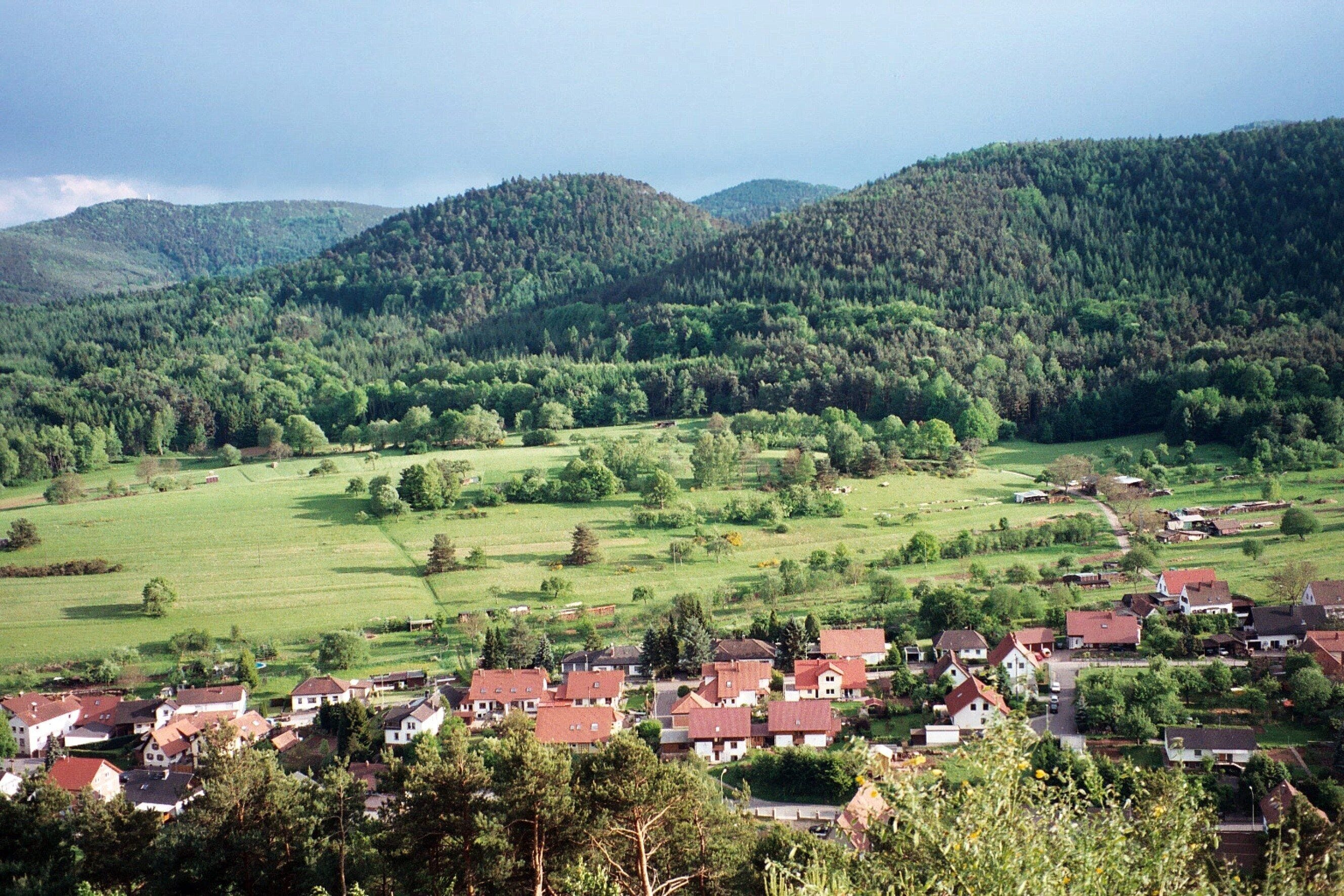 A village nestled in a valley with rolling hills and dense forests in the background.