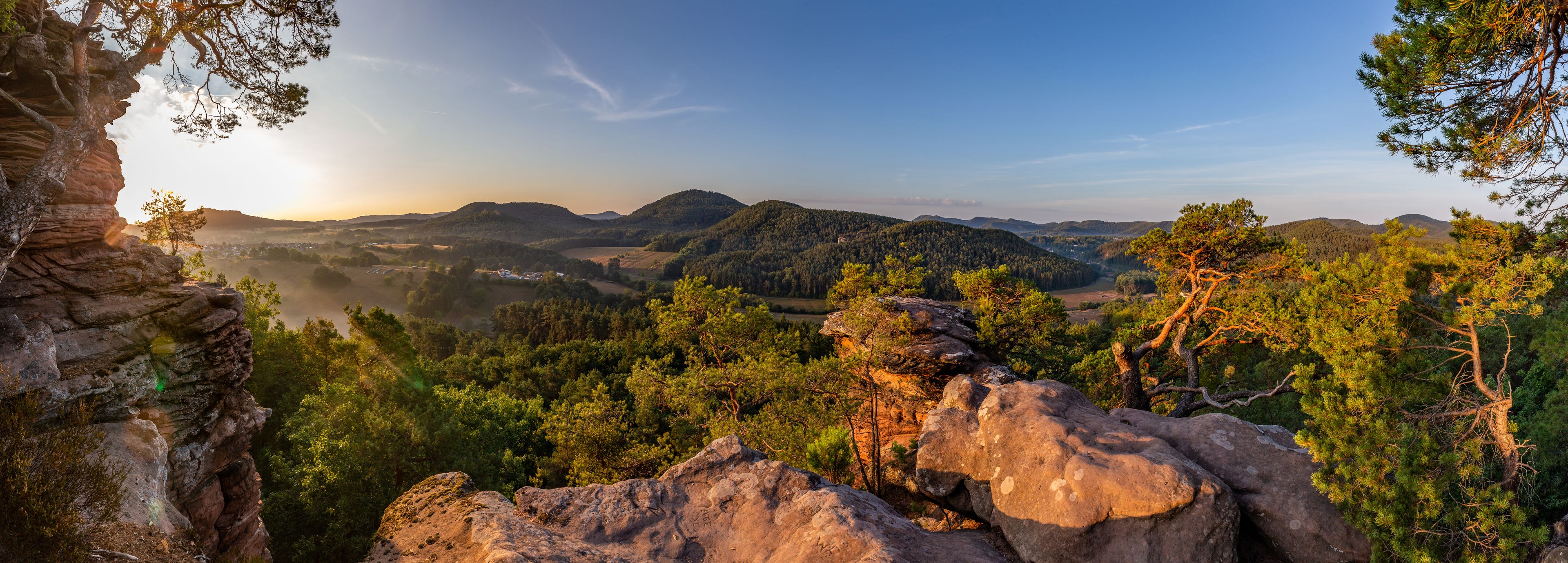 Eine gebirgige Landschaft mit dichten Wäldern, Felsformationen und wolkenlosem Himmel.