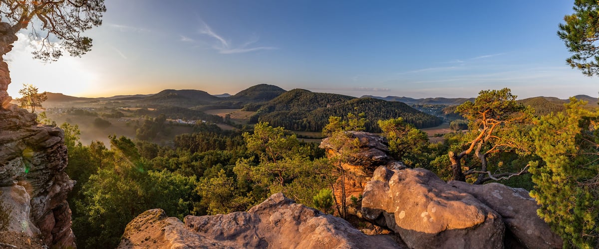 A mountainous landscape with dense forests, rocky outcrops, and a clear sky.