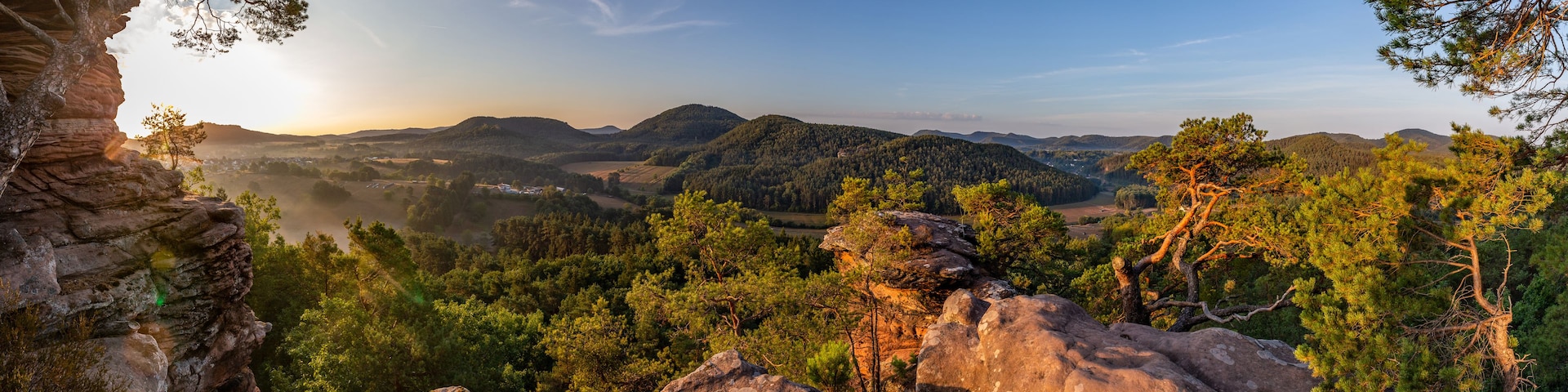 Un paisaje montañoso con bosques densos, afloramientos rocosos y un cielo despejado.