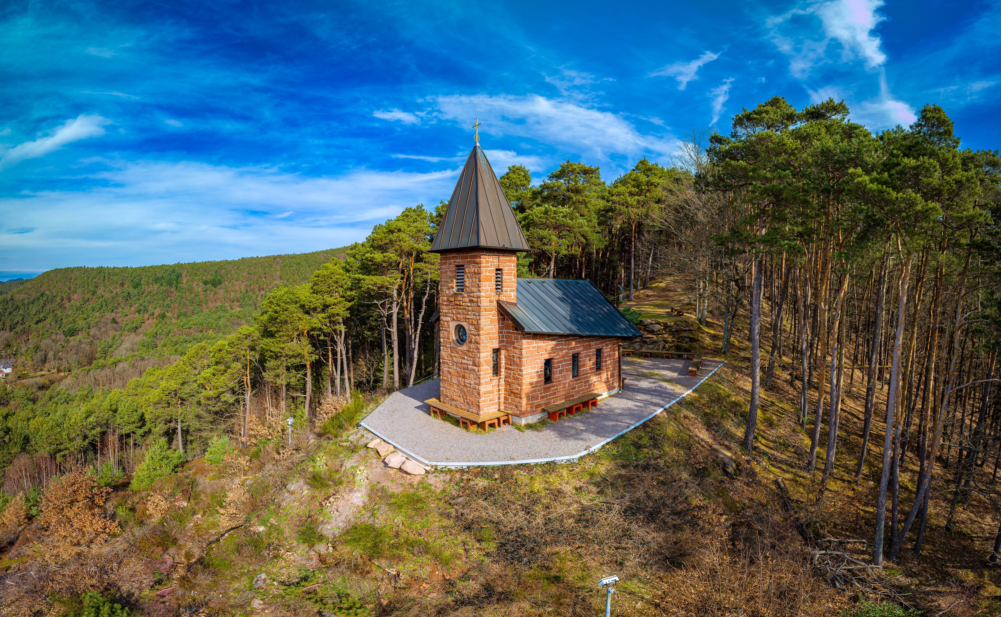 A small church with a bell tower surrounded by a forested hillside.