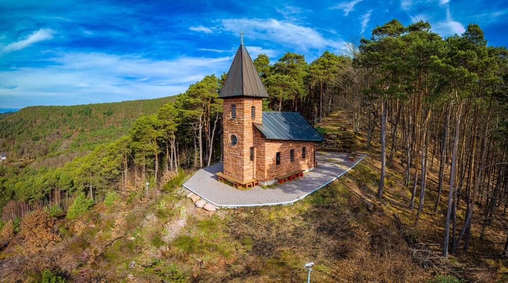 Eine kleine Kirche mit einem Glockenturm, umgeben von einem bewaldeten Hang.