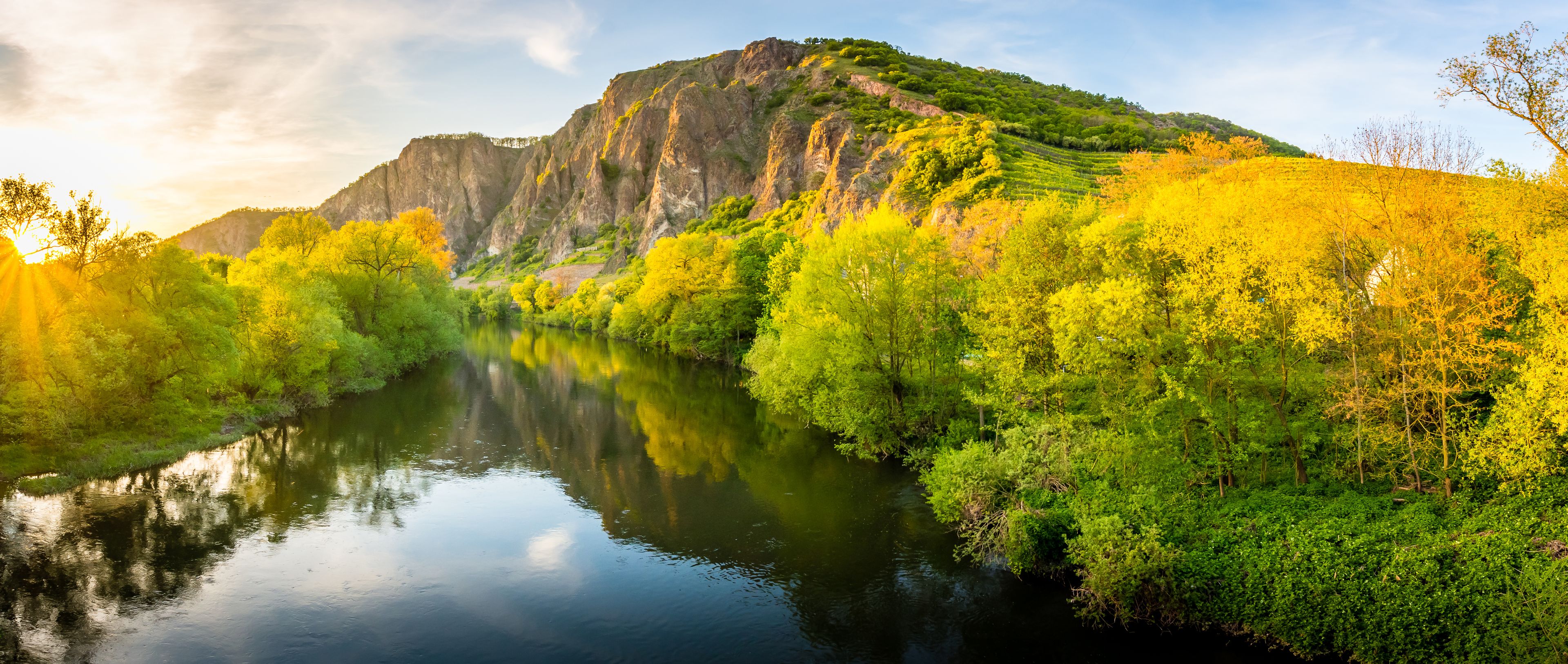 Een rivier die de omliggende begroeiing en een berg op de achtergrond weerspiegelt.