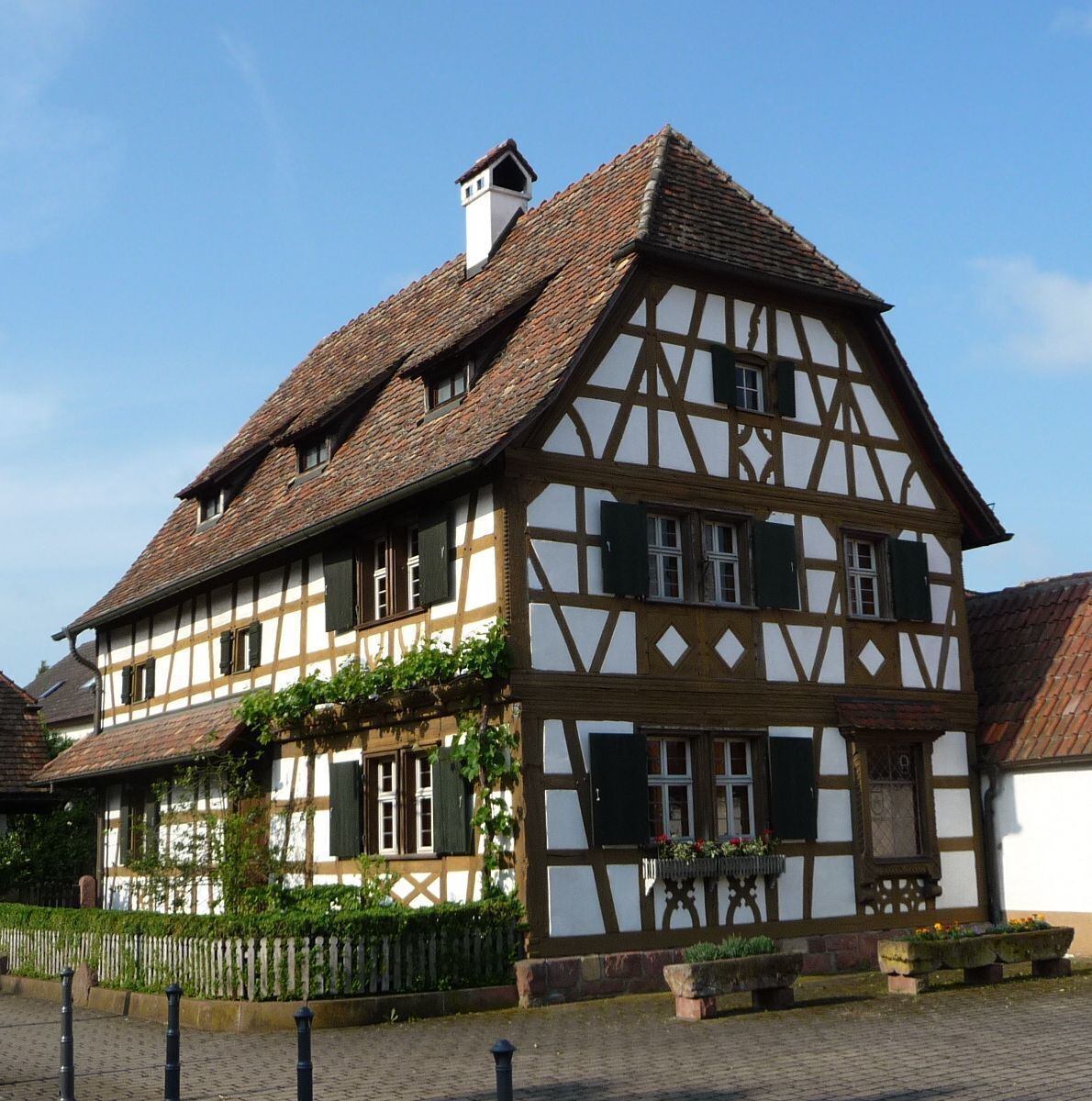 A traditional half-timbered house with a steeply pitched roof, multiple windows with shutters, and a small chimney.