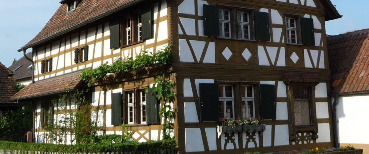 A traditional half-timbered house with a steeply pitched roof, multiple windows with shutters, and a small chimney.