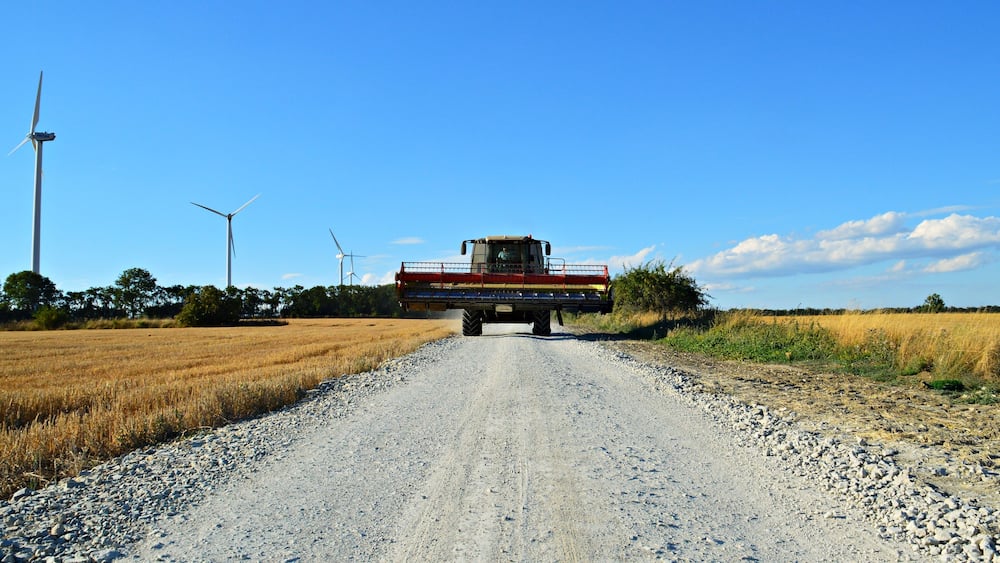 A combine harvester on a gravel road with wind turbines in the background.