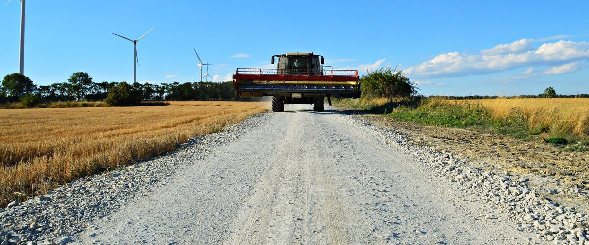 A combine harvester on a gravel road with wind turbines in the background.