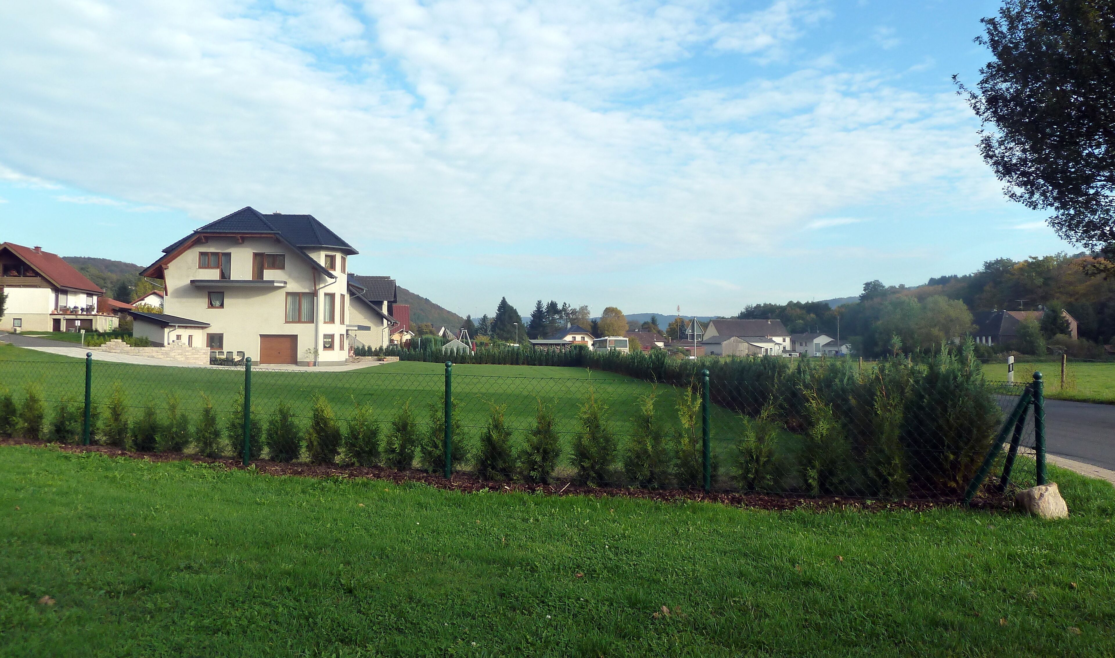 A residential area with houses, a green field, and a fence.