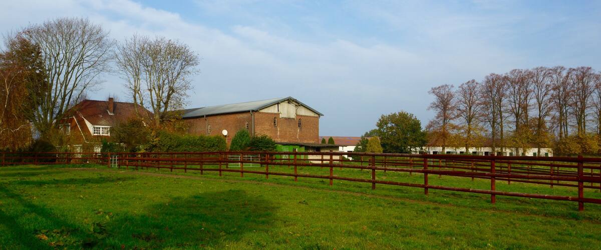 A rural landscape with a large barn, a wooden fence, and a house in the background.