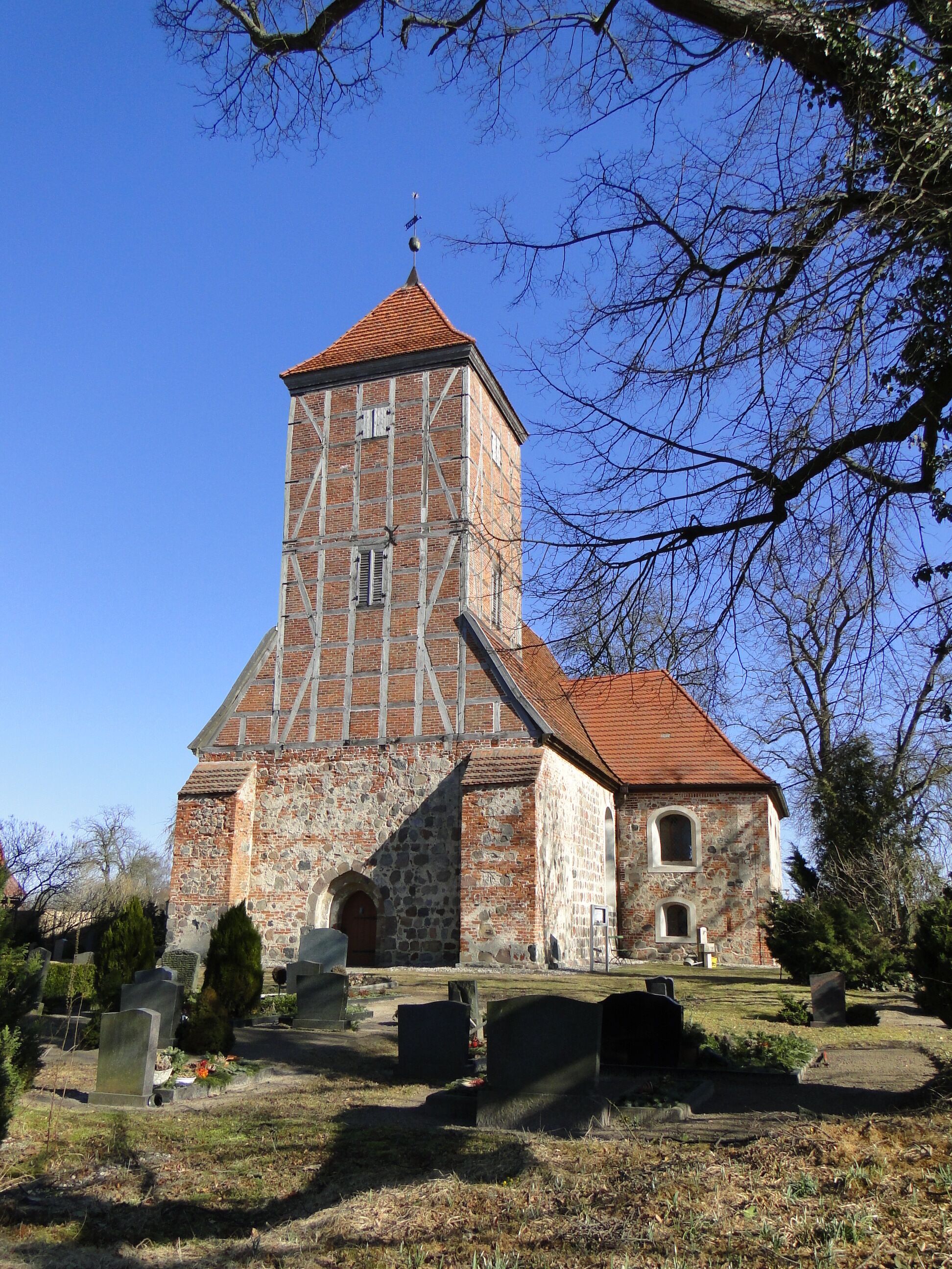 A church with a tall tower and a red roof, surrounded by gravestones and trees.