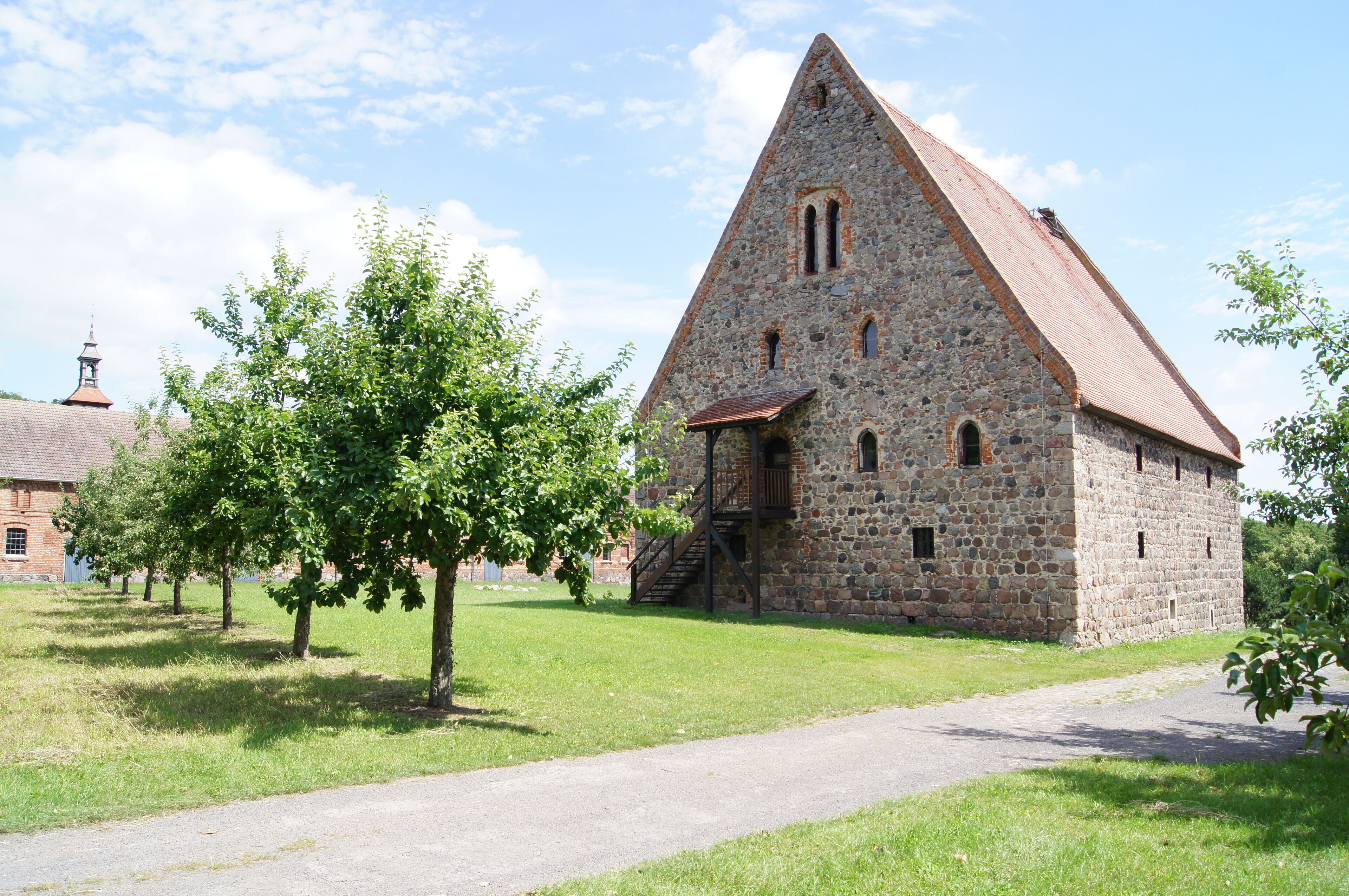 A stone church with a steep roof, surrounded by trees and a clear sky.