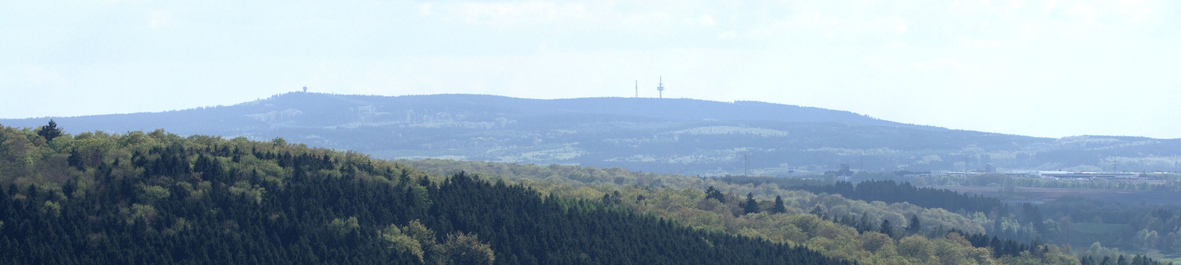 A forested hill with a distant tower and power lines.