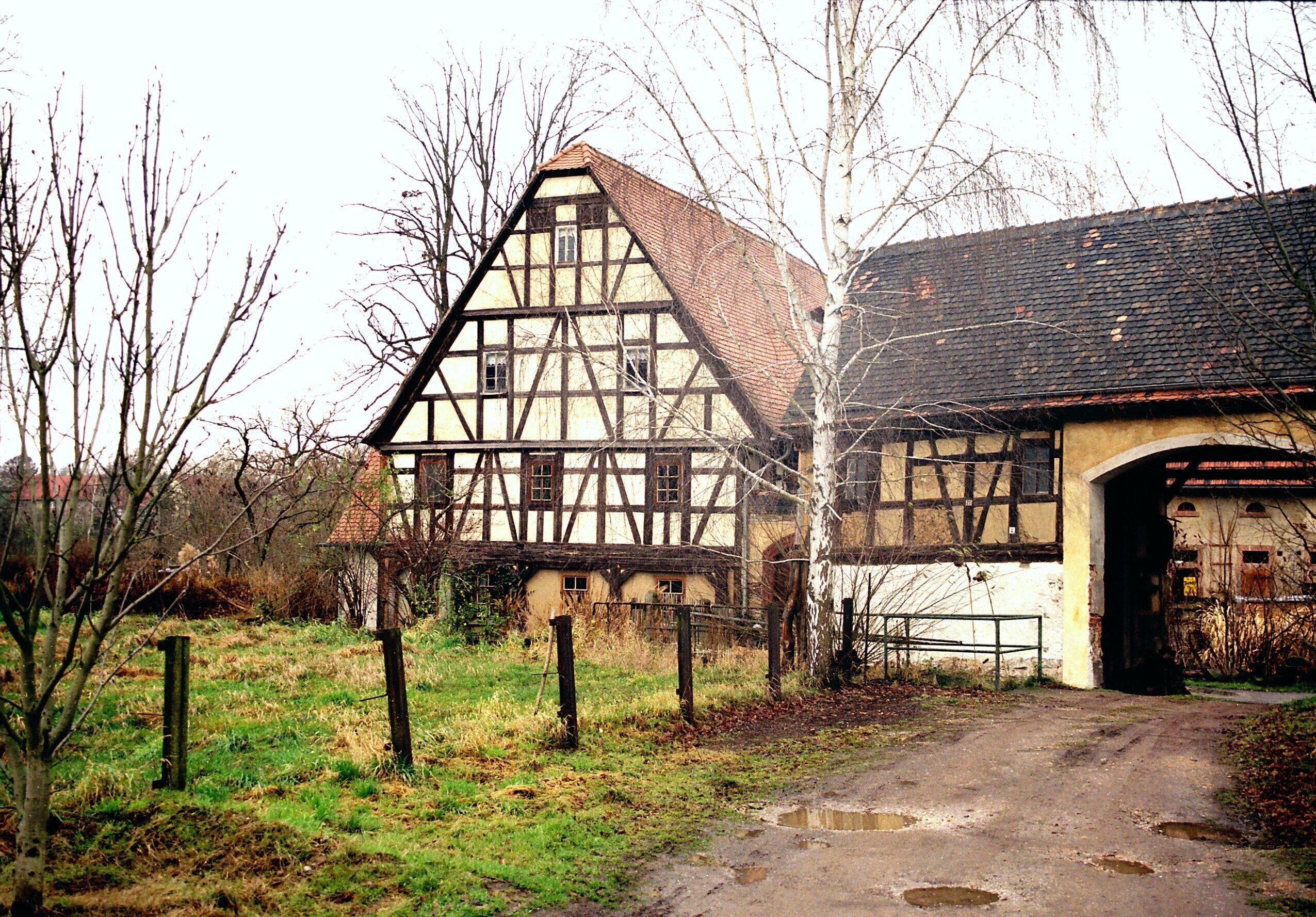 A traditional half-timbered house with a dirt path leading to a barn.