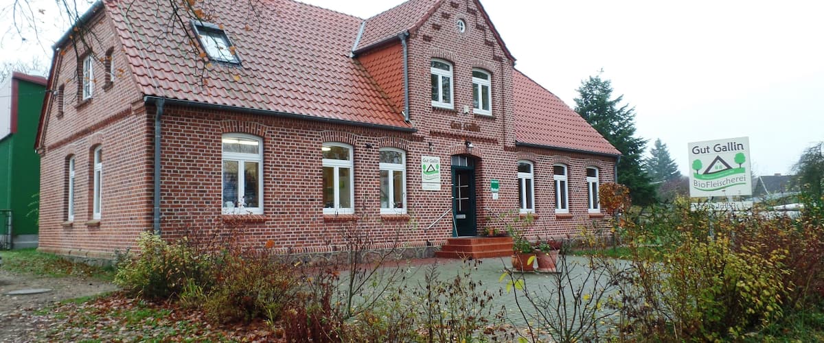 A red brick house with a sloped roof and a sign reading "Gut Gallin Biofleischerei."