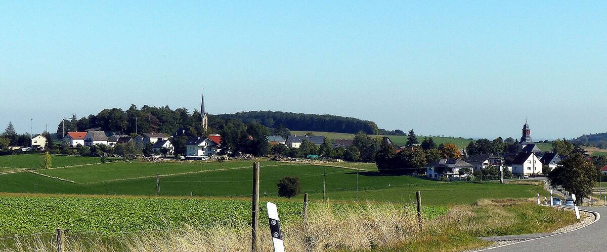A rural landscape with a winding road, green fields, and a church with a tall steeple.