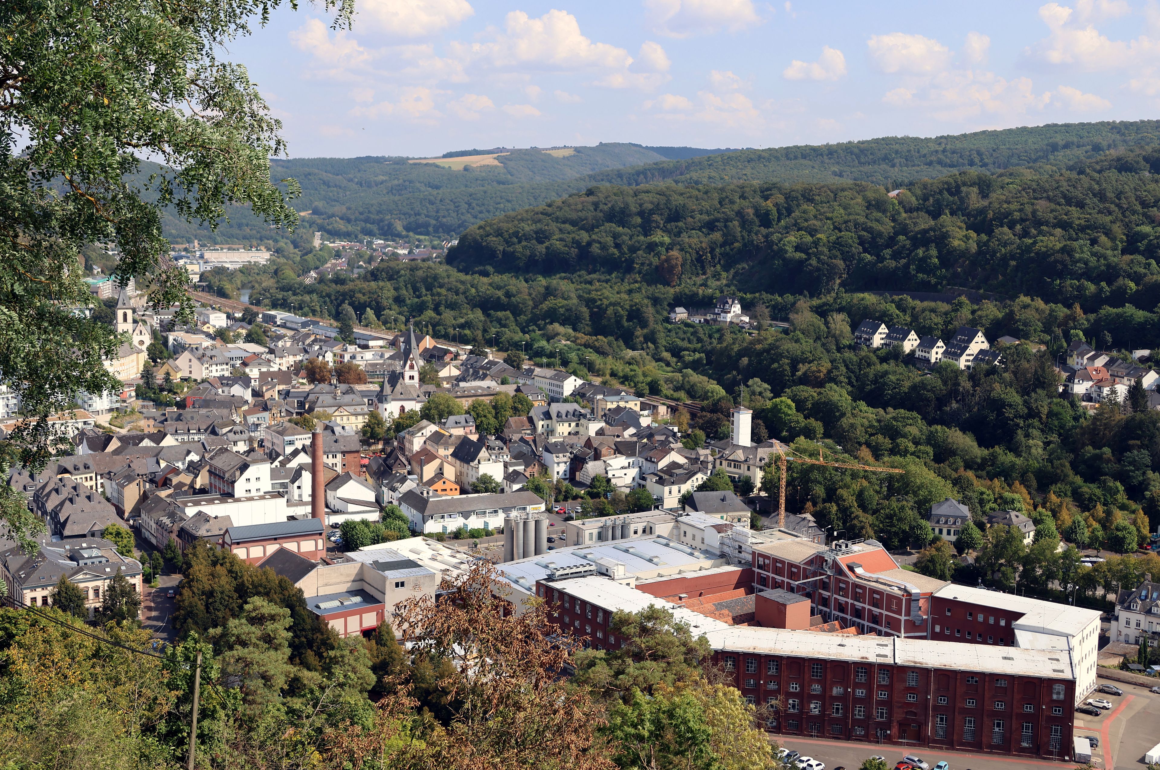 A town nestled in a valley with a prominent church tower, surrounded by dense forests and rolling hills.