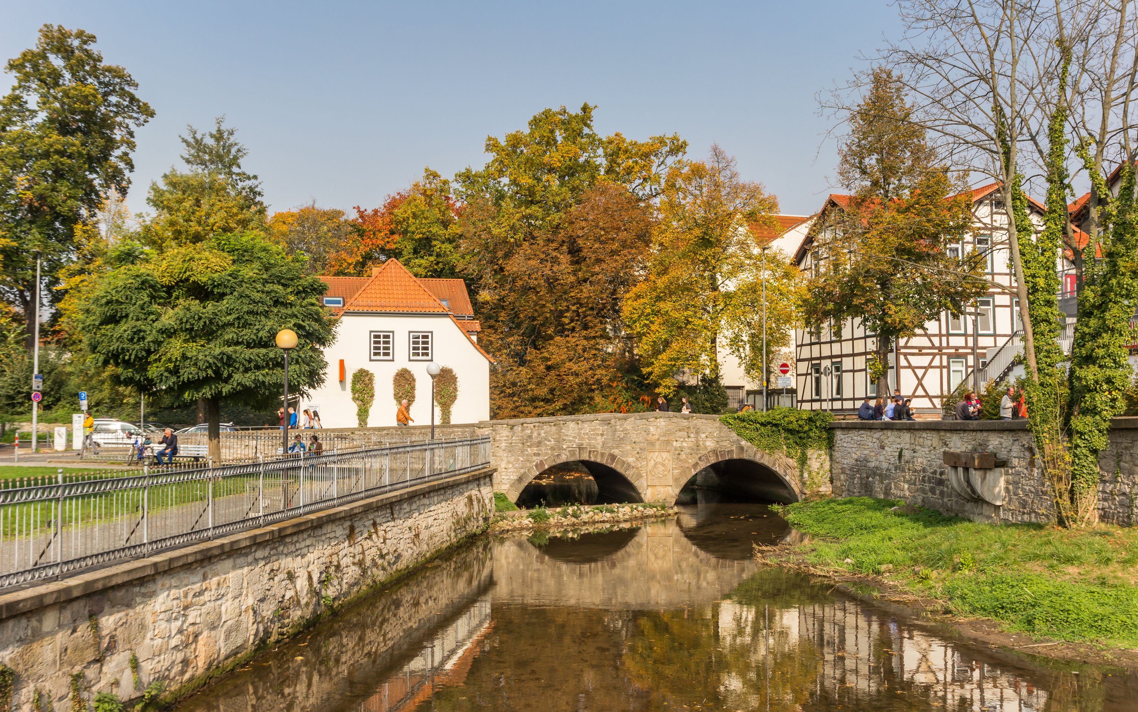 A stone bridge over a canal with a white building and trees in the background.