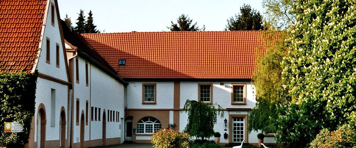 A traditional building with a red-tiled roof, surrounded by a well-maintained garden with grass, shrubs, and a few white birds.