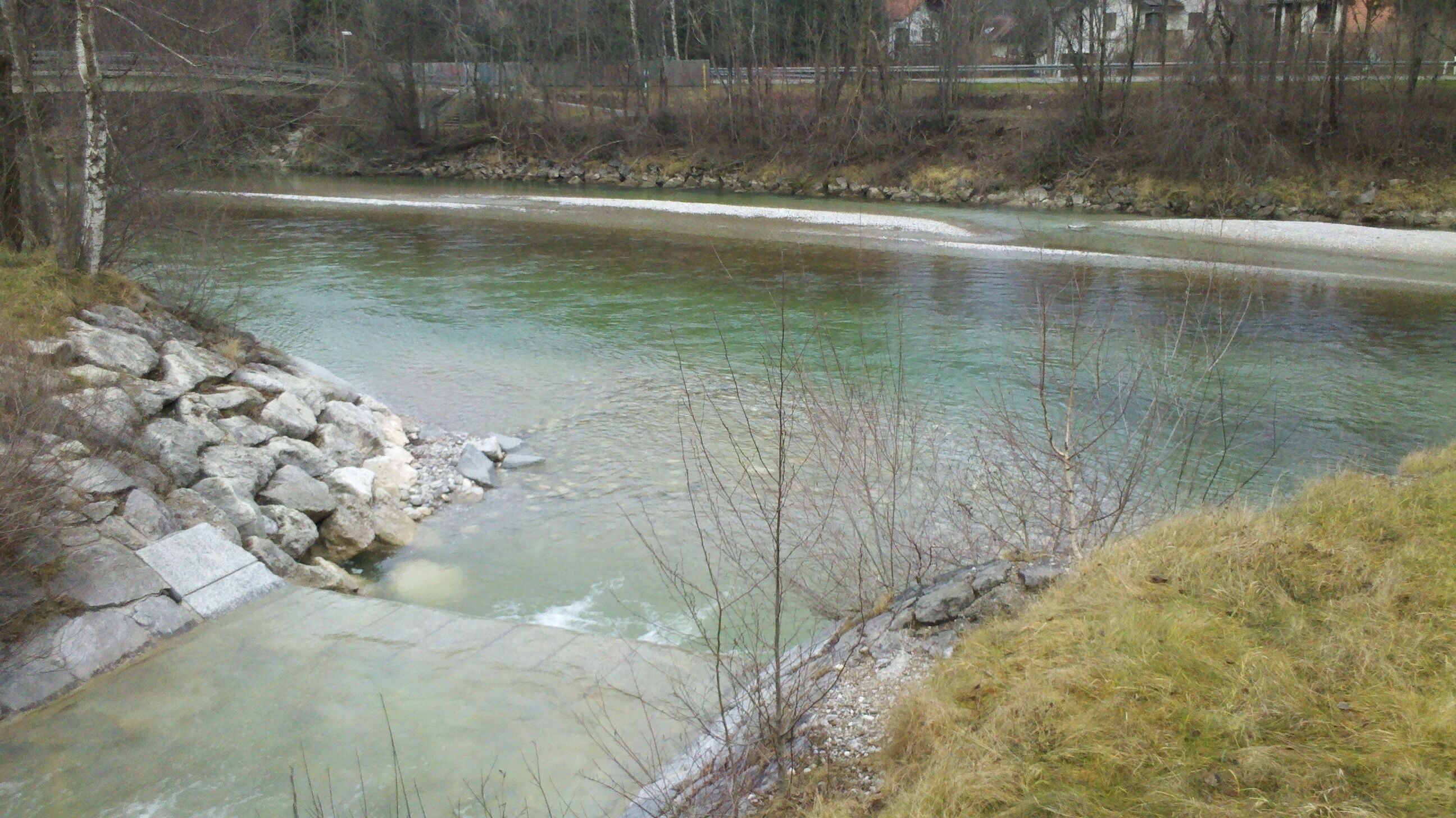 A river with clear water, surrounded by rocks and sparse vegetation.