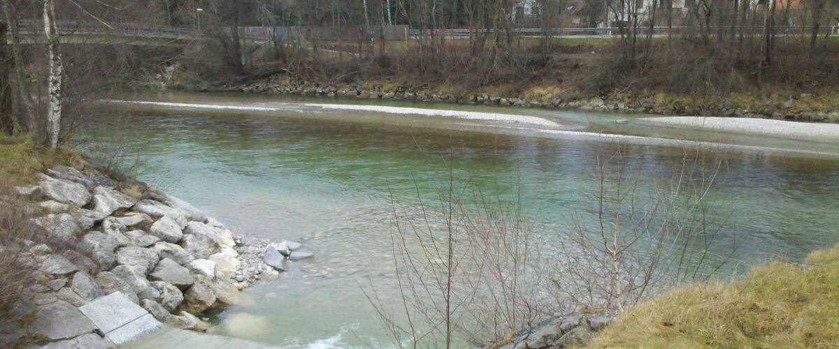 A river with clear water, surrounded by rocks and sparse vegetation.