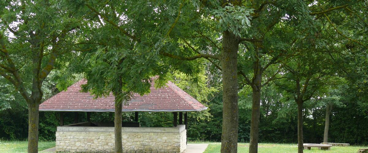 A gazebo with a stone wall and a red roof surrounded by trees and grass.