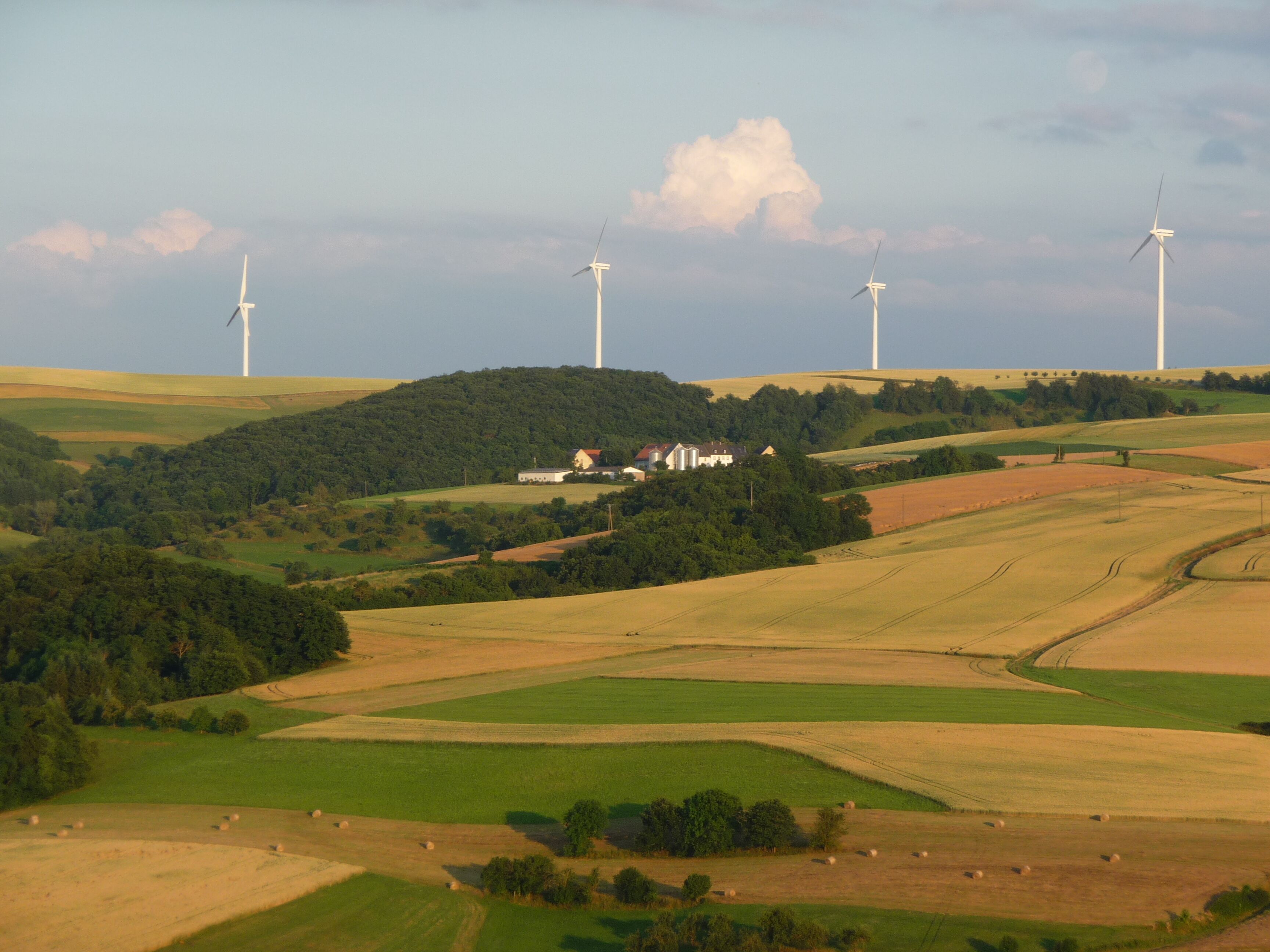 A landscape with wind turbines, rolling hills, and scattered buildings.
