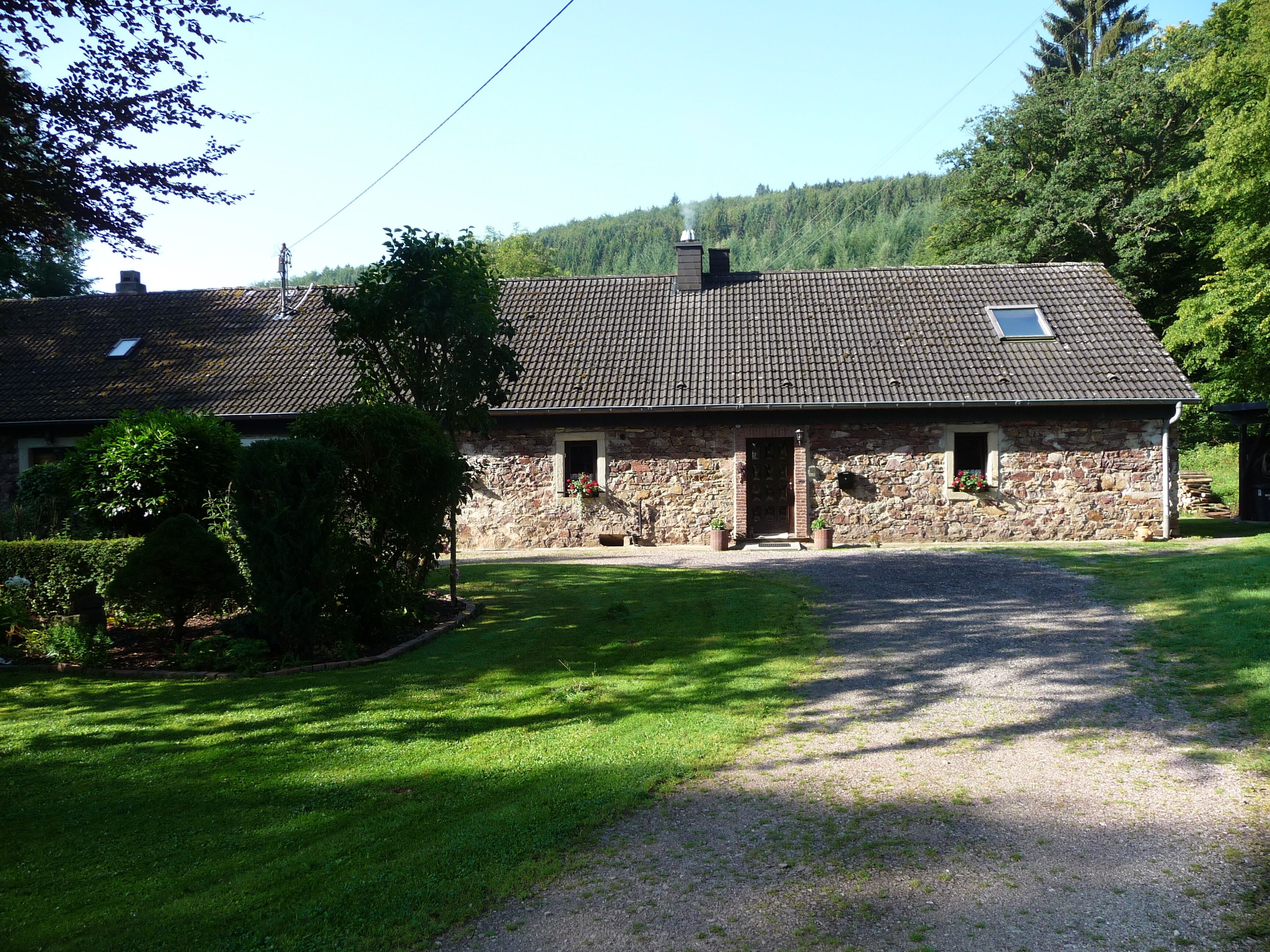 A stone house with a tiled roof, surrounded by a well-maintained lawn and trees.