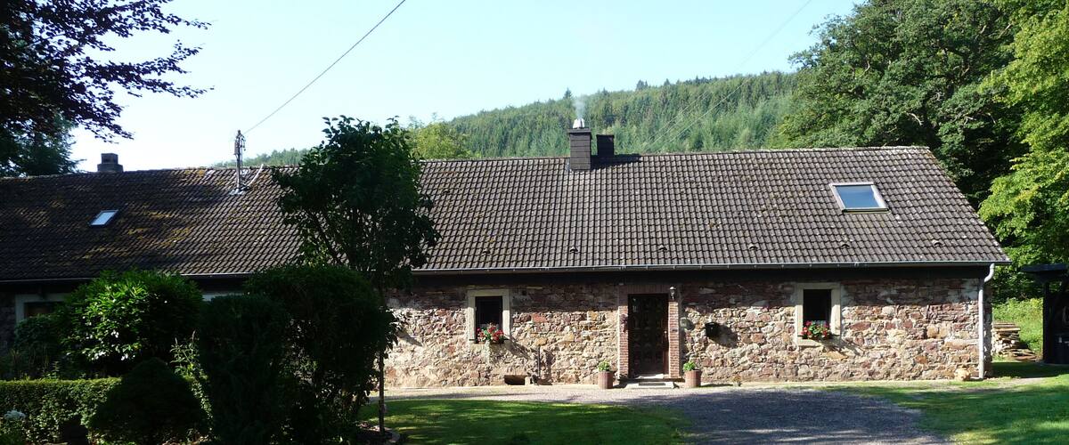 A stone house with a tiled roof, surrounded by a well-maintained lawn and trees.