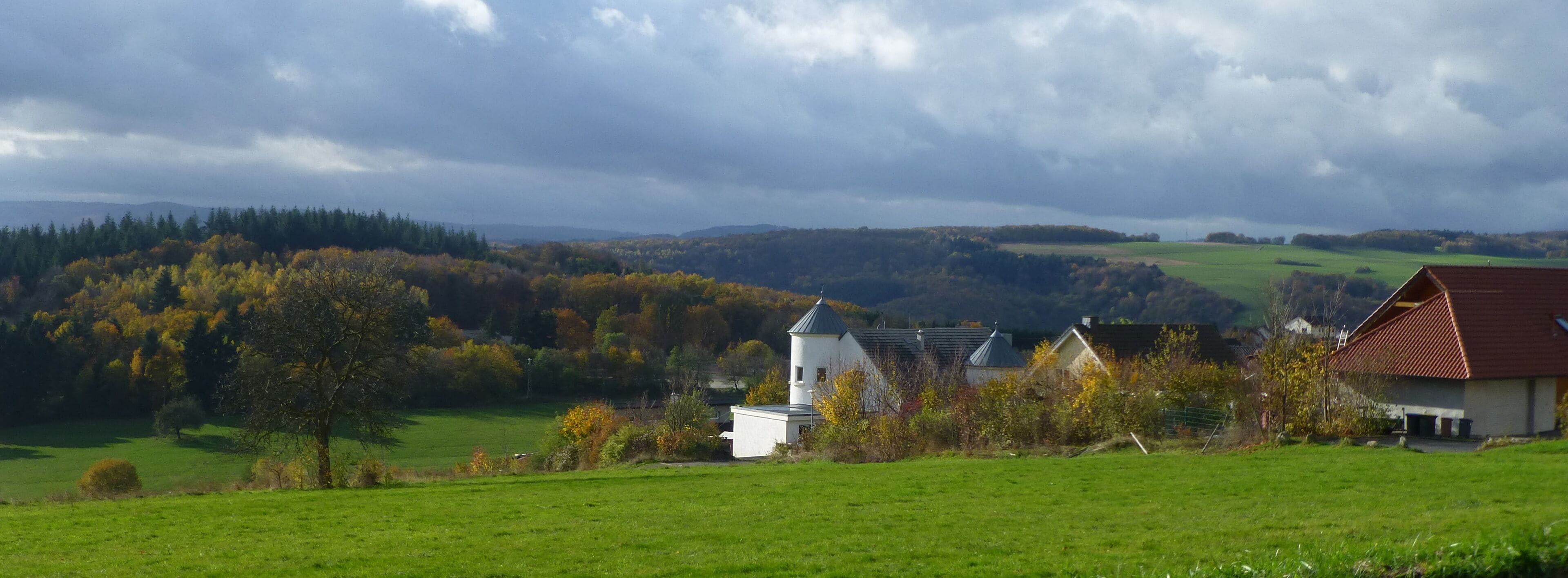 A rural landscape with a white church, a red-roofed house, and autumn-colored trees.