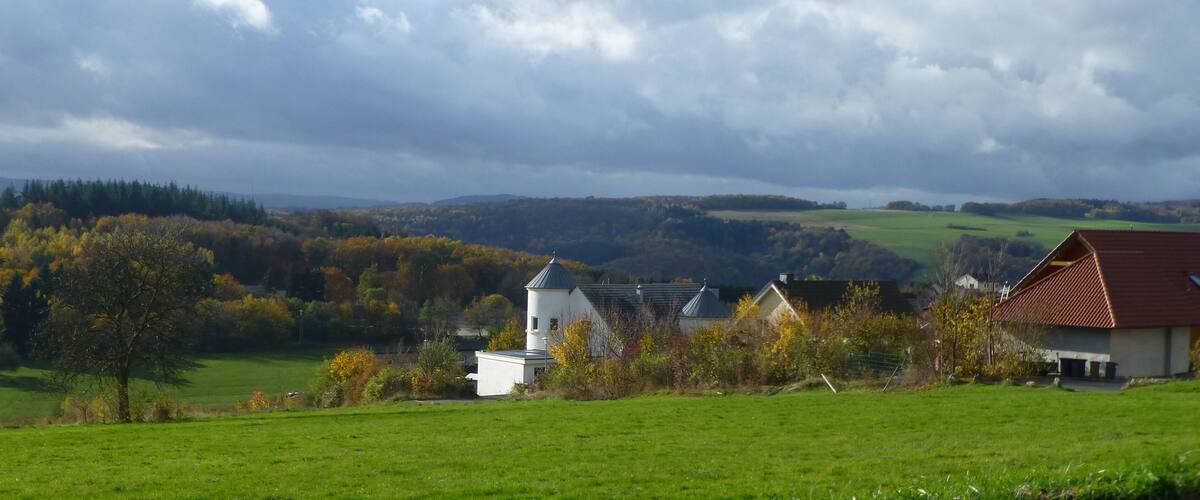 A rural landscape with a white church, a red-roofed house, and autumn-colored trees.