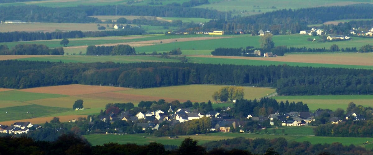 A rural landscape with rolling fields, scattered houses, and dense forests.