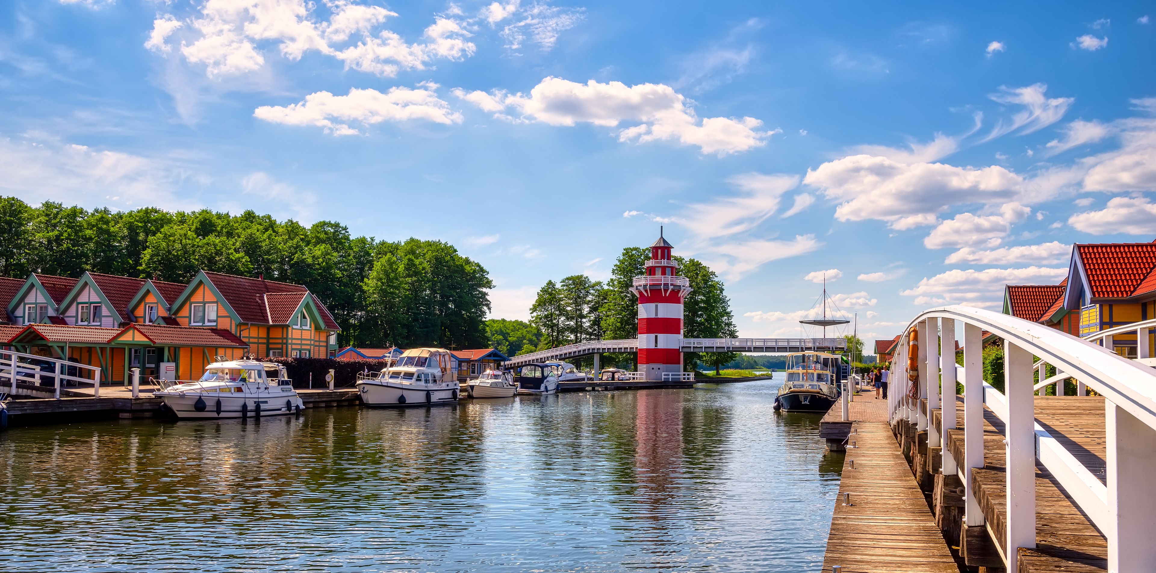 A canal with boats, a red and white lighthouse, and colorful houses along the water.