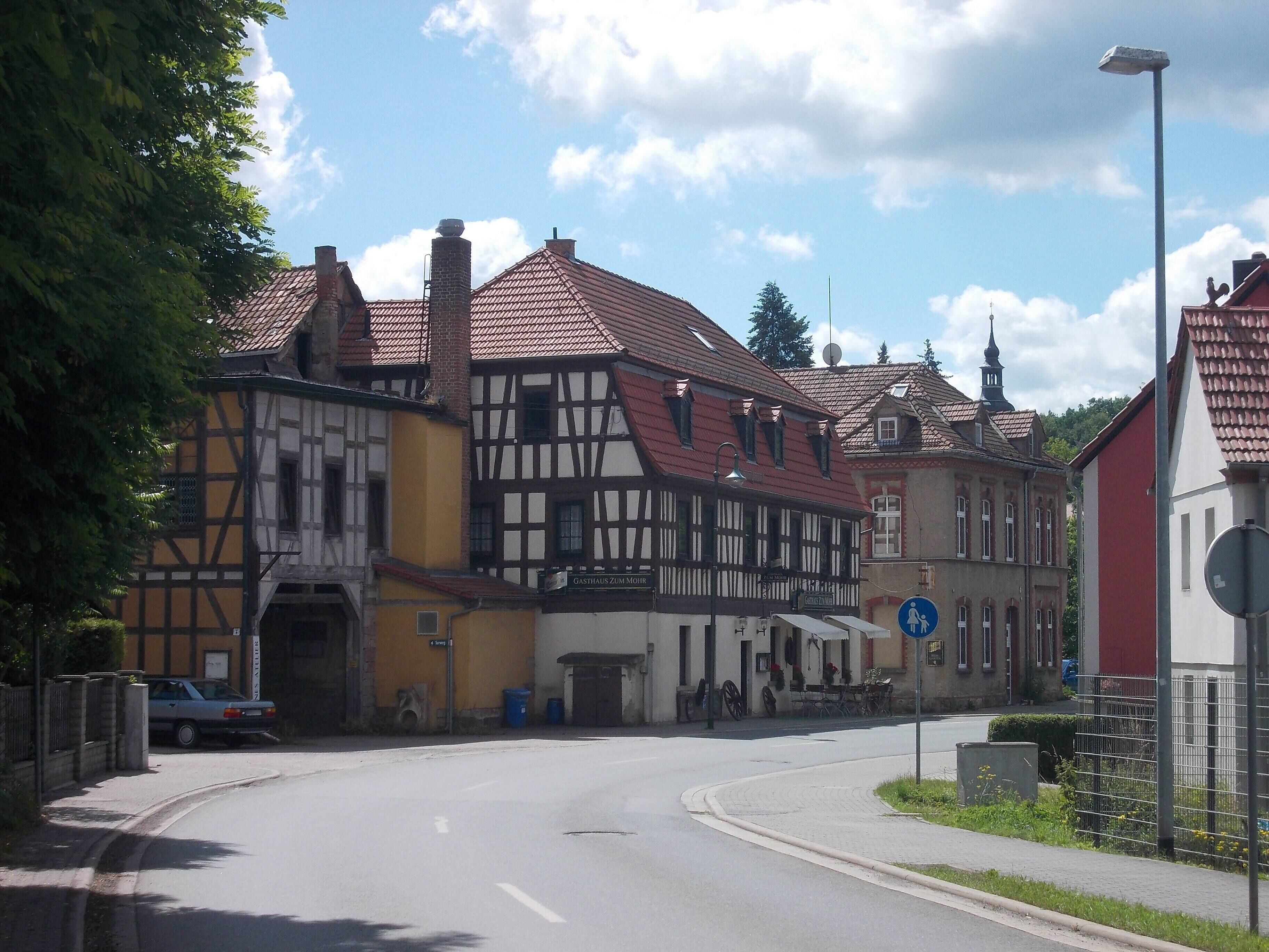A street with traditional half-timbered houses, a clear blue sky, and a pedestrian crossing sign.