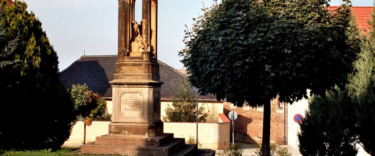 A stone monument with inscriptions, surrounded by trees and a cobblestone path.