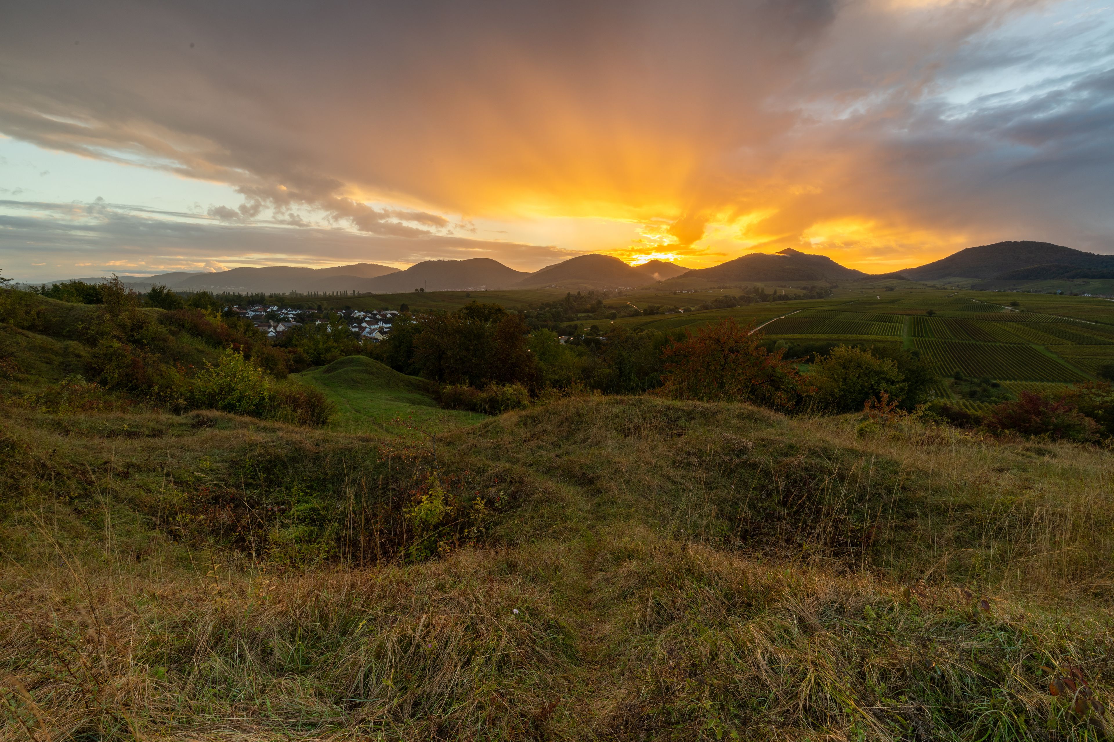 A sunset over rolling hills with a village in the valley.