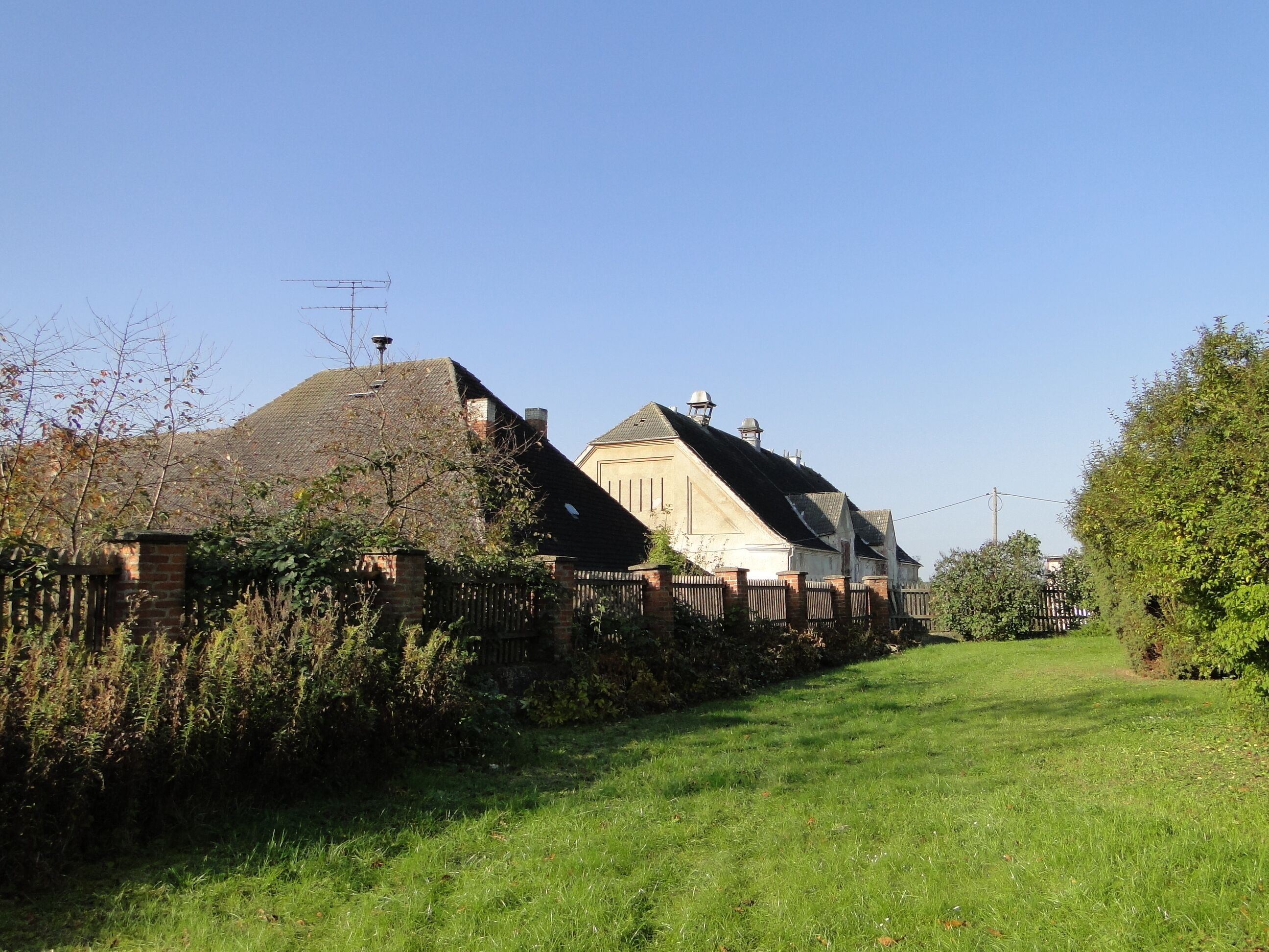 A rural landscape with a thatched-roof house, a white house with a gabled roof, and a clear blue sky.