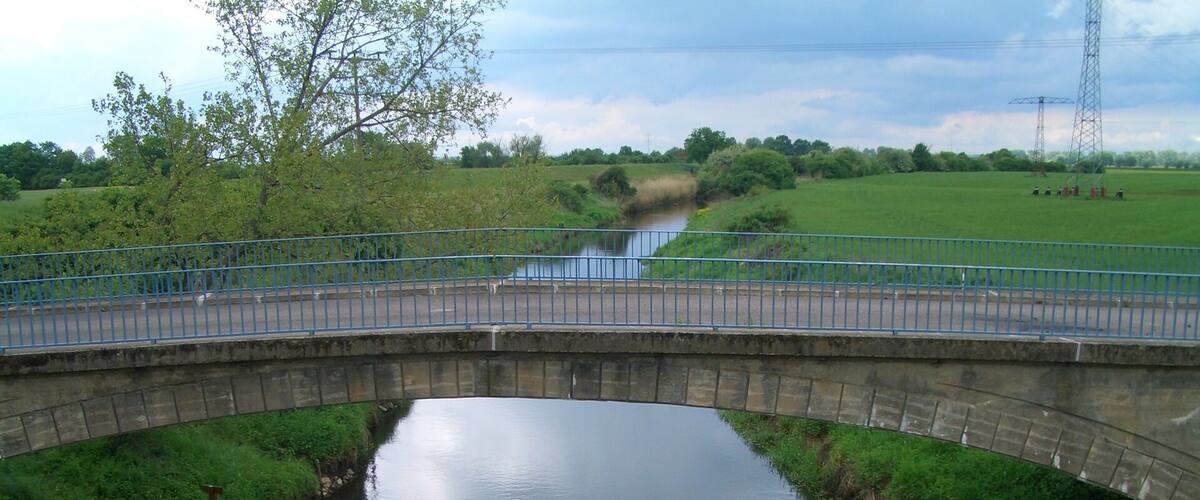 A stone bridge over a calm river with grassy banks and trees.