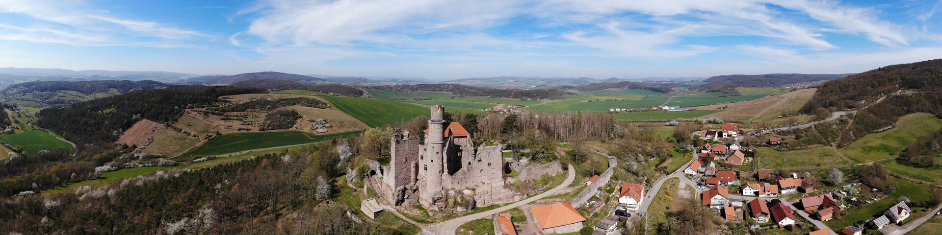 Un château médiéval entouré d’un village, de collines verdoyantes et d’un ciel dégagé.