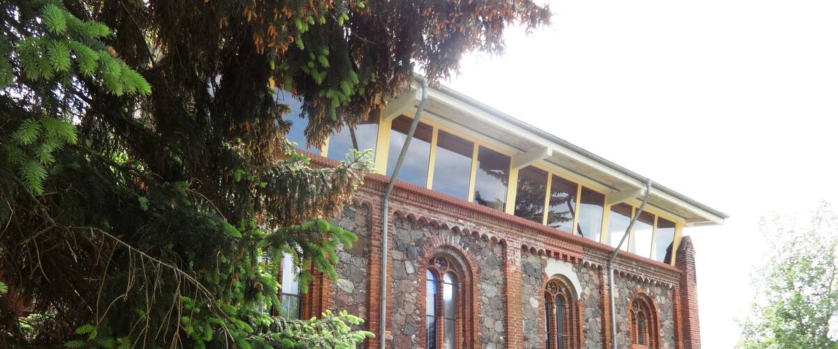 A historic building with arched windows and a stone facade, surrounded by a well-maintained lawn and trees.