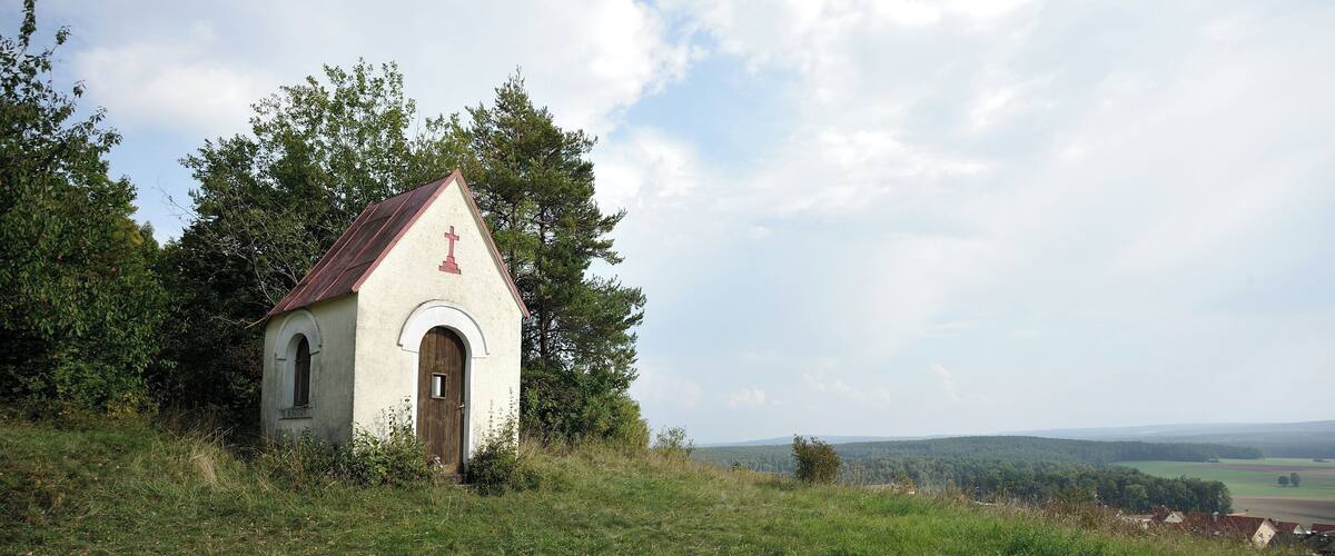 A small white church with a red cross on the roof, surrounded by green grass and trees.