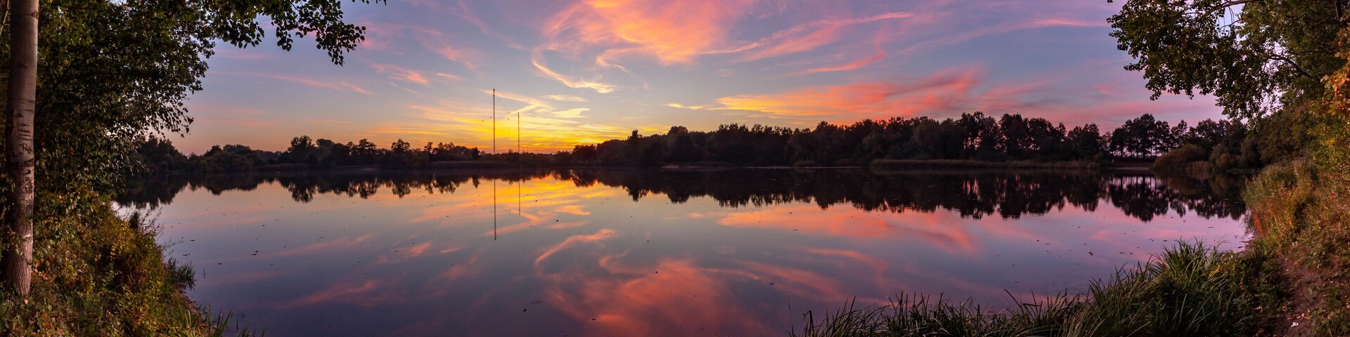 Un lago tranquilo con el reflejo de un atardecer, rodeado de árboles y un cielo despejado.