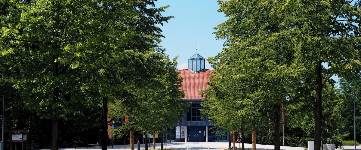 A tree-lined pathway leading to a building with a red roof and a blue sign reading "RATHA".