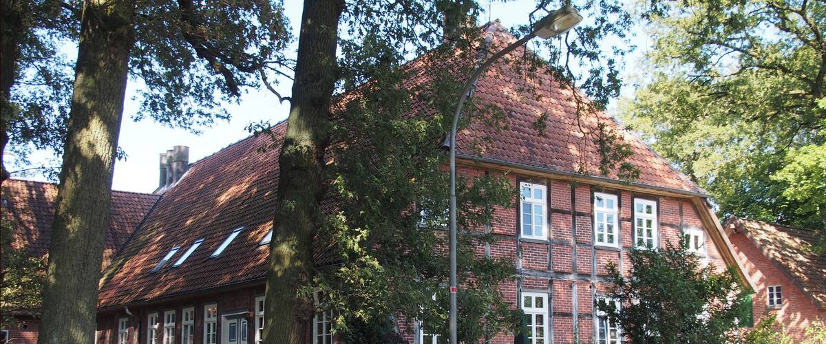 A red brick house with a sloped roof, surrounded by trees and a wooden fence.