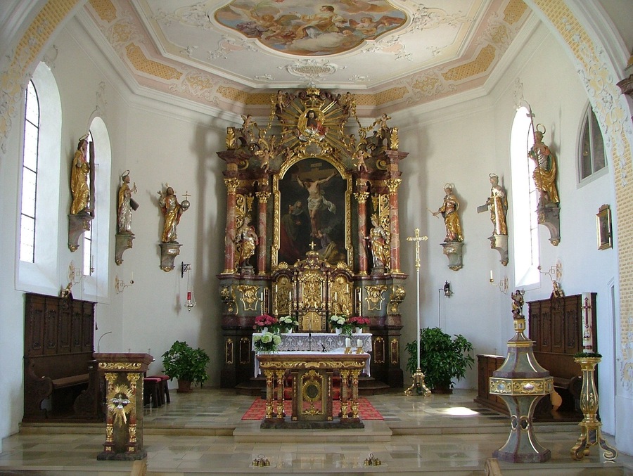 Interior de iglesia ornamentado con un altar central, estatuas y un techo detallado.