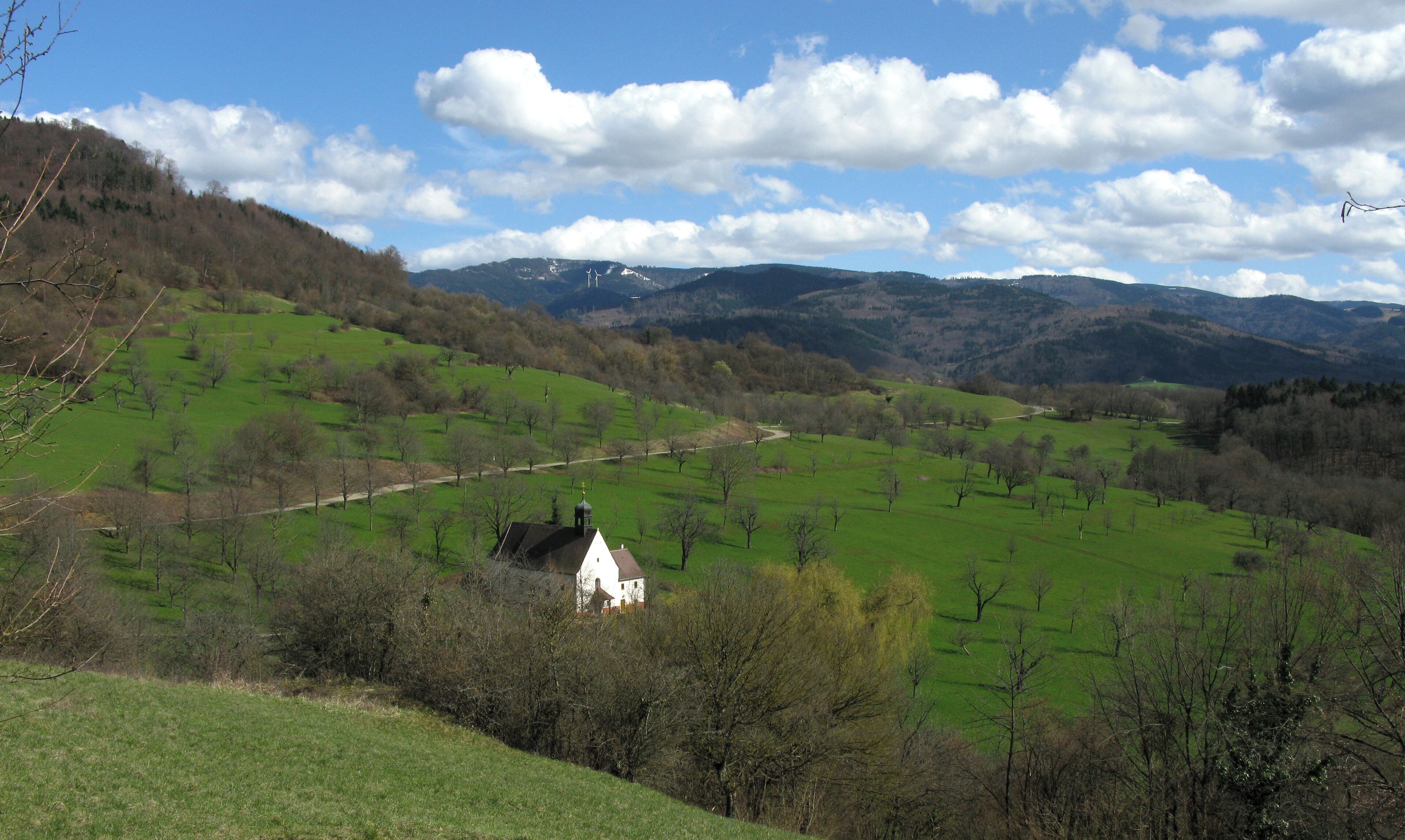 A white house on a green hillside with a clear sky and mountains in the background.