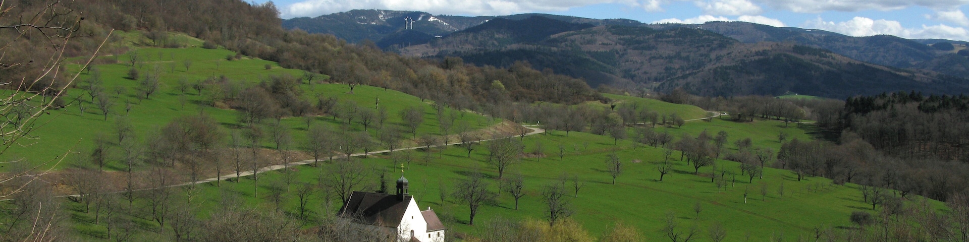 A white house on a green hillside with a clear sky and mountains in the background.