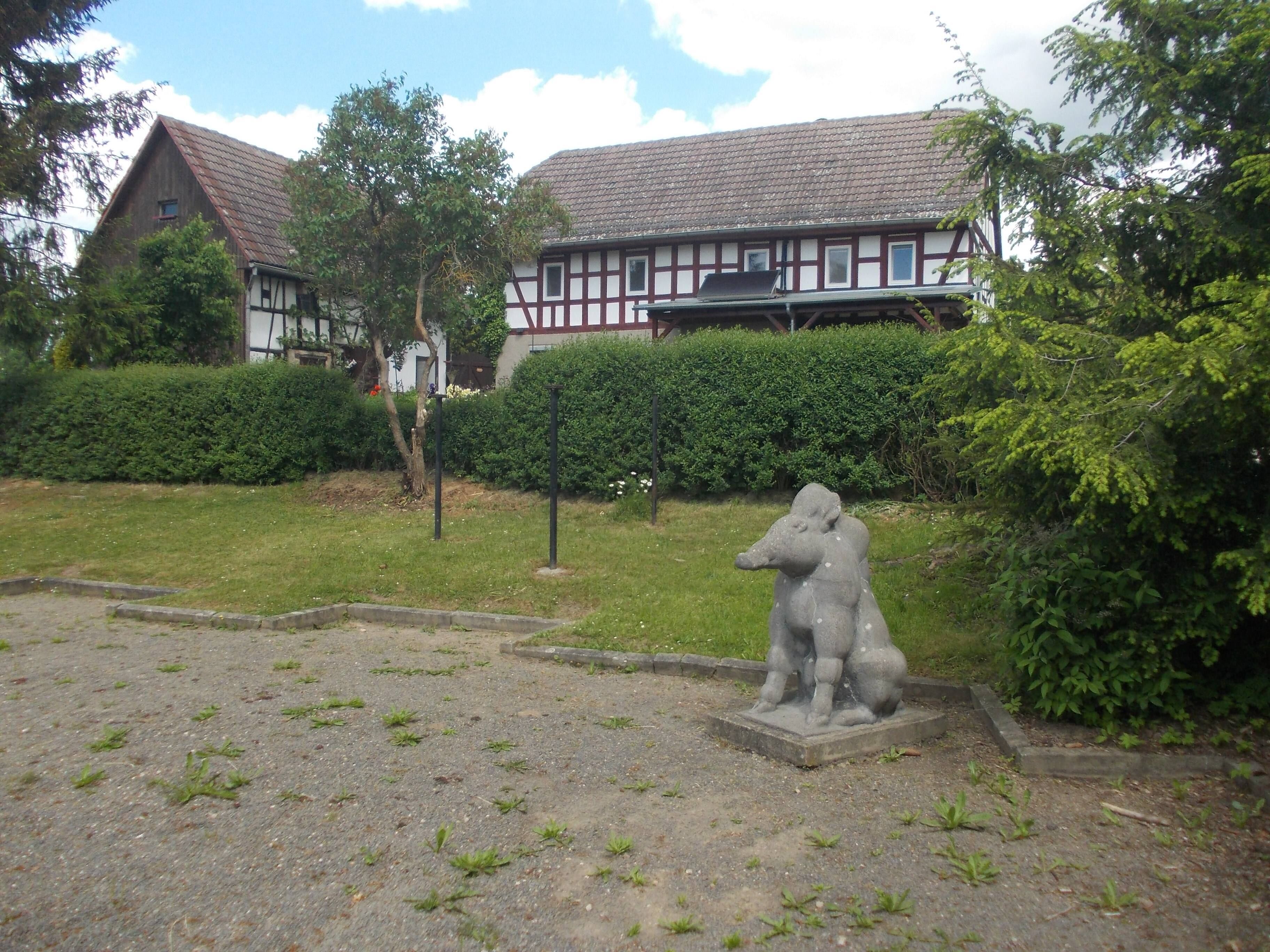 A courtyard with a statue, a hedge, and a building with a tiled roof.